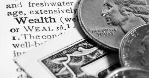 A close-up view of a dictionary entry for the word "wealth," with coins and dollar bills sitting on the page.