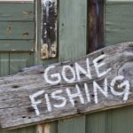 On a weathered olive-green door hangs a gnarled wooden sign that reads "gone fishing" in white paint.