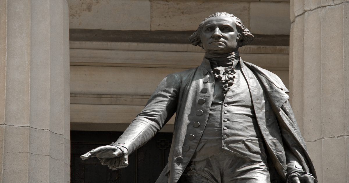 A George Washington statue outside of a limestone building. The statue has a brushed steel finish with minute details.