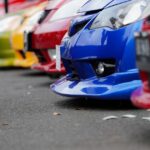 A low-angle side view captures a row of differently colored cars parked bumper-to-bumper in a shaded environment.