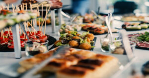 A food station at a large event with various height displays and finger foods spread out. The tablecloth is white.